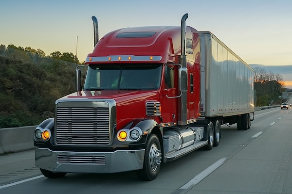 Red semi-truck tractor trailer 18 wheeler on highway at sunrise